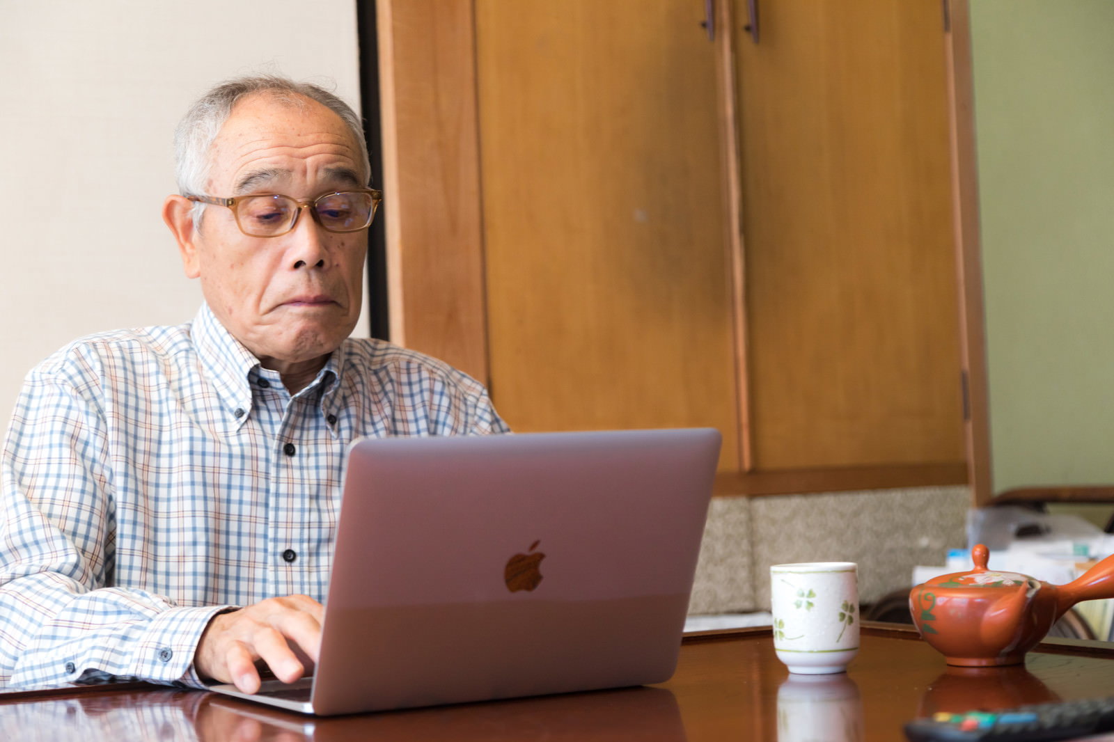 自宅でMacBookを操作する高齢男性［モデル：まーちゃん］