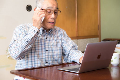 電話しながらパソコンを操作するシニア男性