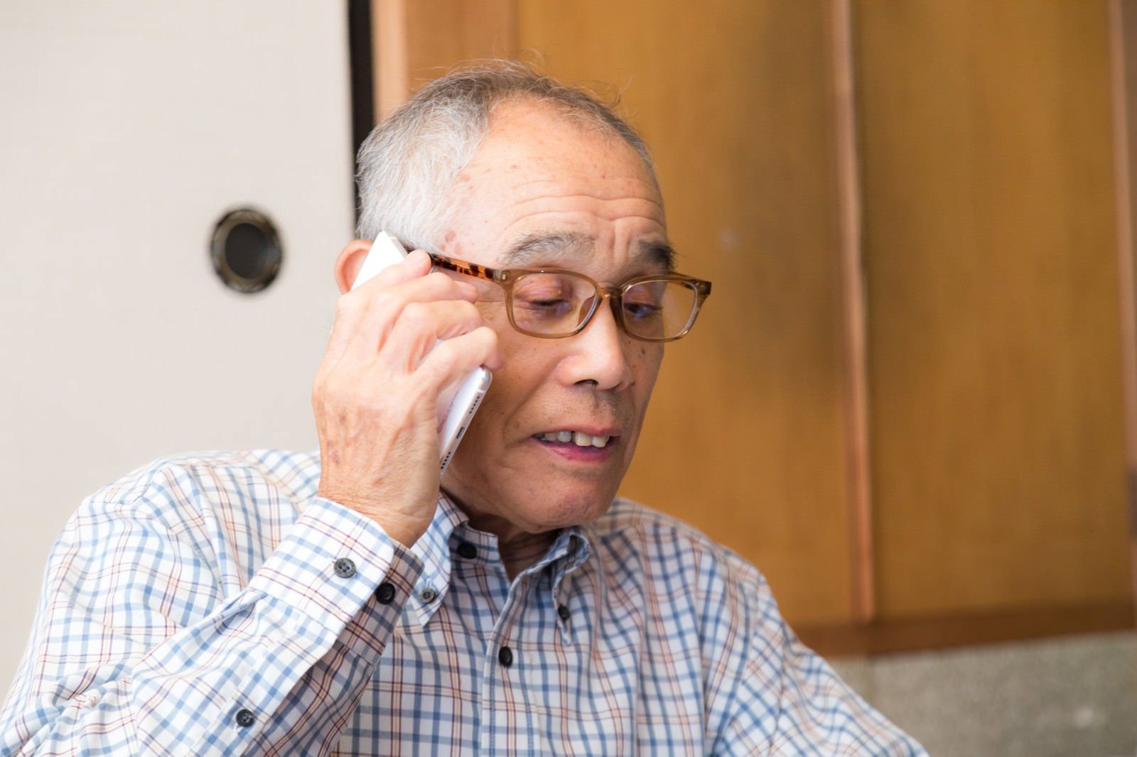 チェックシャツを着た眼鏡の高齢男性が電話で通話している様子［モデル：まーちゃん］