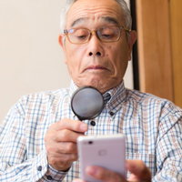 携帯の画面が小さくて拡大鏡を使うおじいさんの写真