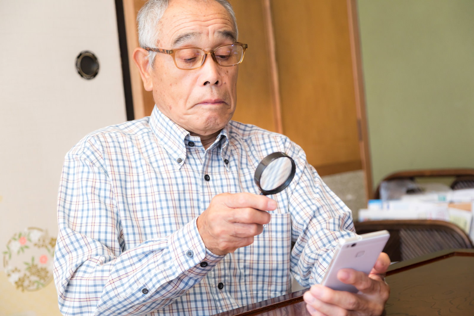 ルーペを使って携帯電話の文字を確認している高齢男性［モデル：まーちゃん］