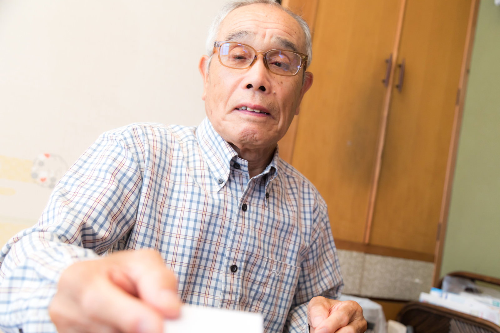 チェック柄のシャツを着たおじいさんがお年玉の封筒を差し出している［モデル：まーちゃん］