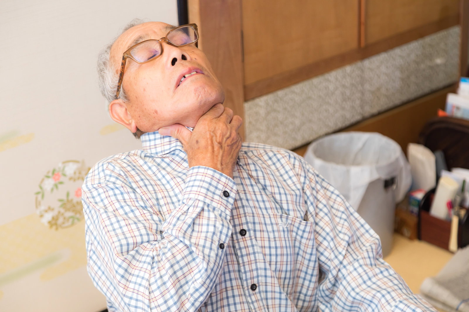 誤飲して喉に詰まって苦しそうな表情で両手で喉を押さえる高齢男性［モデル：まーちゃん］