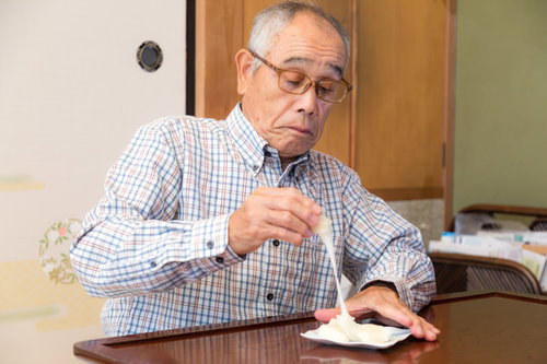手づかみで伸びるお餅を食べようとする爺さんの食事風景