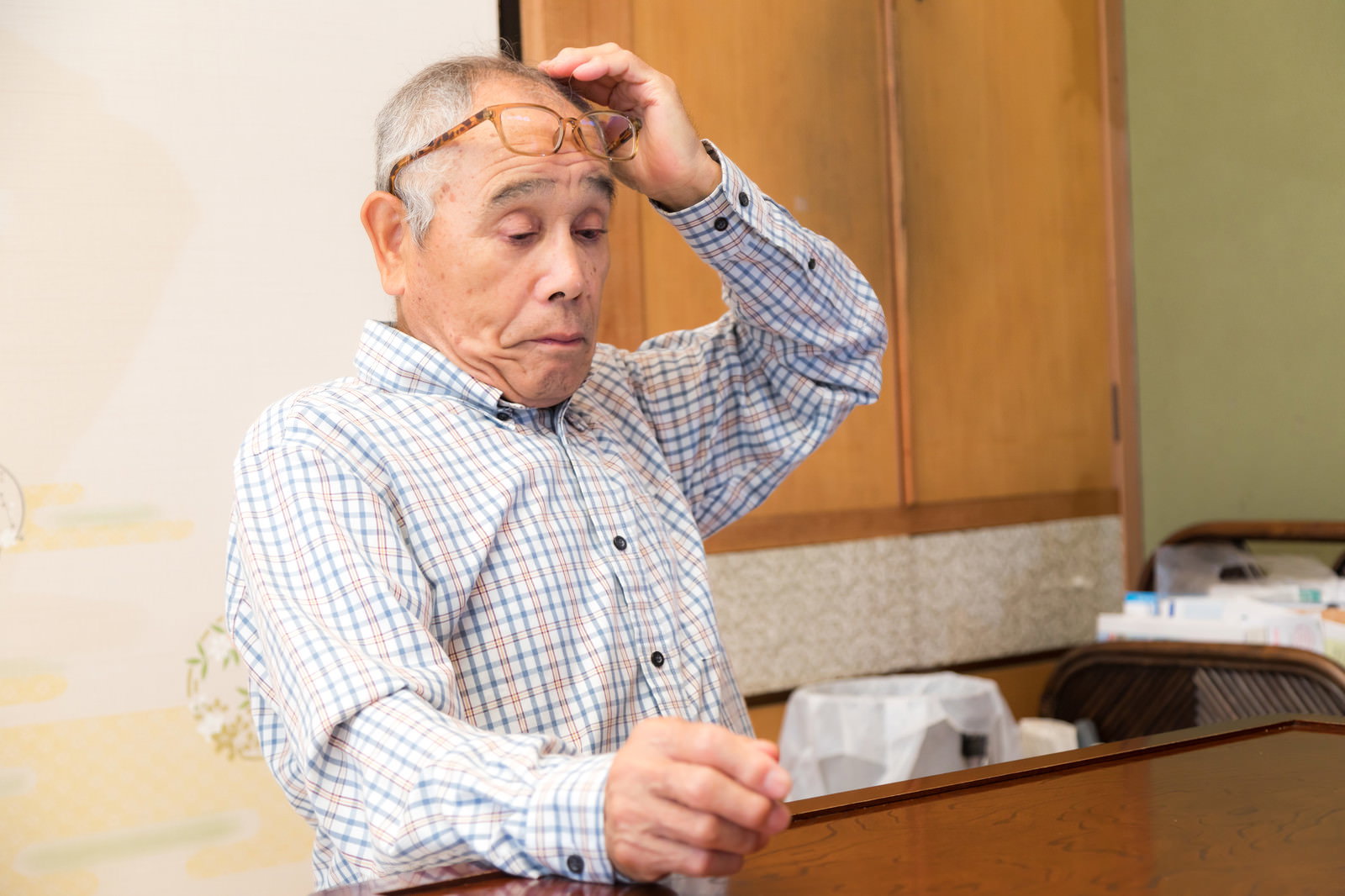 額に手を当てて困った表情で考え込むメガネをかけた男性［モデル：まーちゃん］