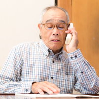 通販カタログを見ながら電話注文する高齢男性の写真