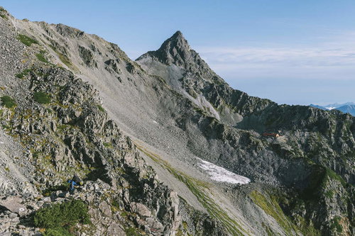 晴天の空の下、岩峰がそびえ立つ槍ヶ岳の山頂と登山者
