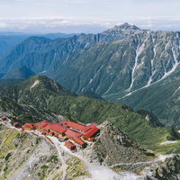 赤い屋根の槍ヶ岳山荘と笠ヶ岳の遠景、北アルプスの雄大な山々の写真