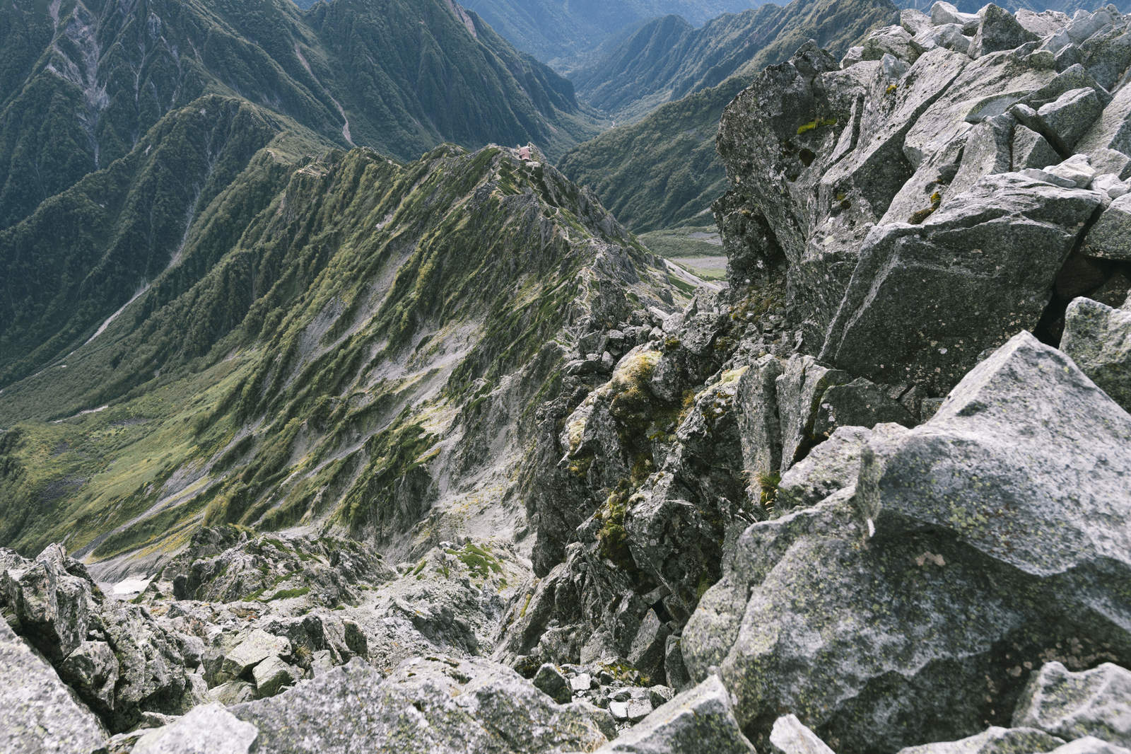 槍ヶ岳山頂の岩場から東鎌尾根と北アルプスの山並みを望む