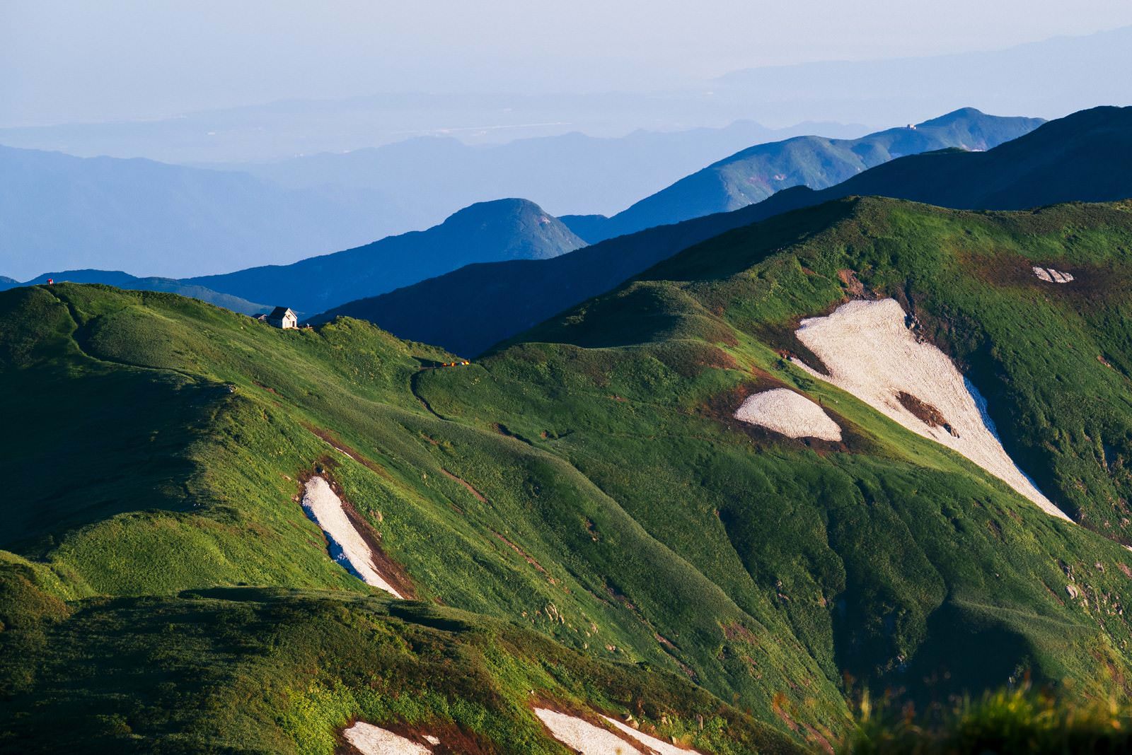明け方の緑の稜線に囲まれた白い門内小屋の遠景