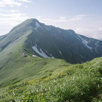 飯豊山の緑の稜線に建つ梅花皮小屋遠景と登山道の写真