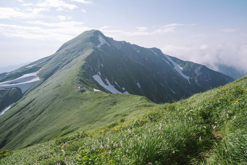 飯豊山の緑の稜線に建つ梅花皮小屋遠景と登山道