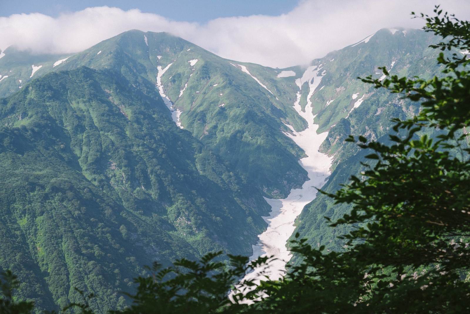 緑深い飯豊山の山並みと石転び沢の谷間、白い残雪が見える山岳風景
