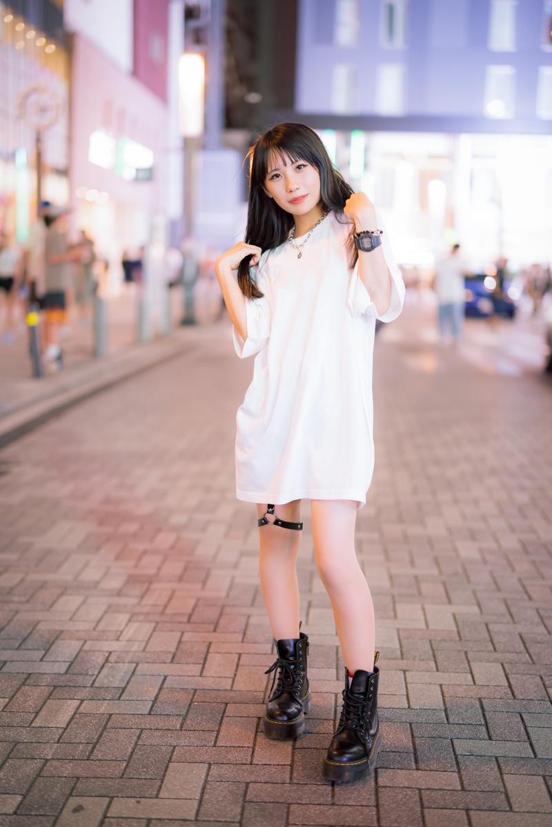 白いオーバーサイズTシャツと黒ブーツを着た女性が夜の街で立つ［モデル：るい］