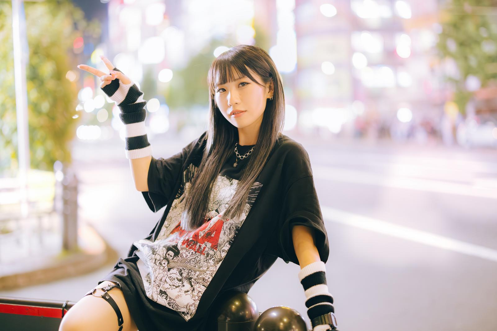夜の繁華街で片手ピースをする女子の写真素材［モデル：るい］