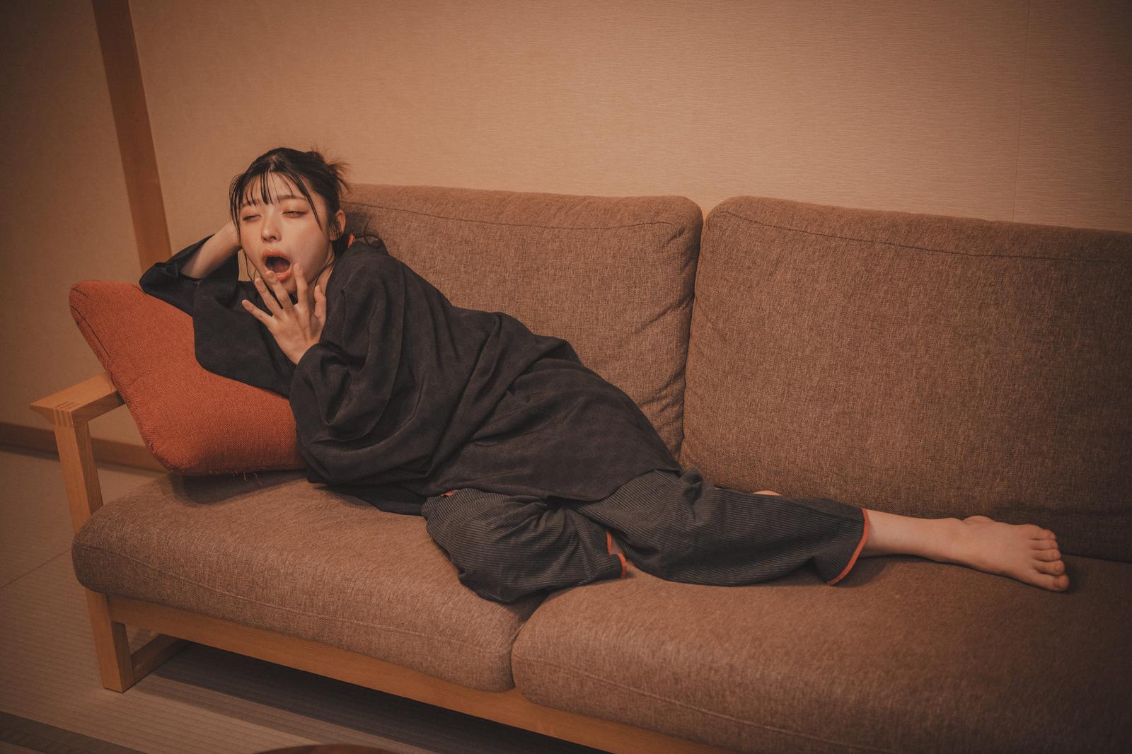 ソファーの上であくびをして眠気に襲われている女性［モデル：高尾実生］