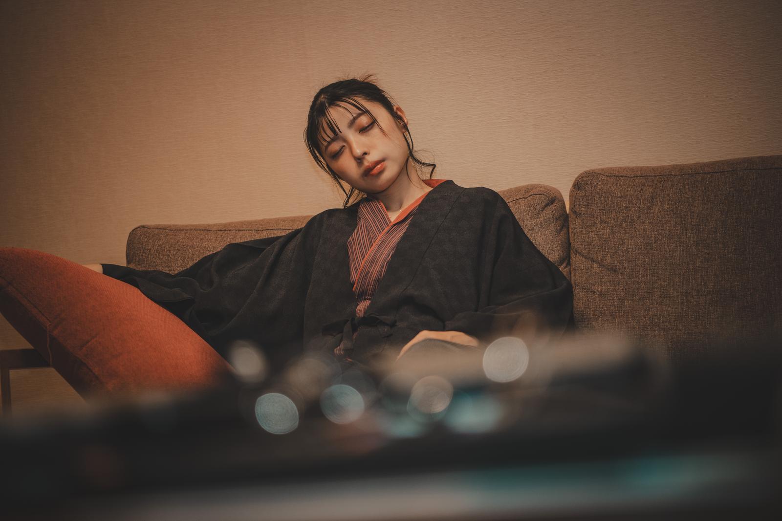 ソファーで目を閉じて眠る黒いジャケット姿の女性［モデル：高尾実生］