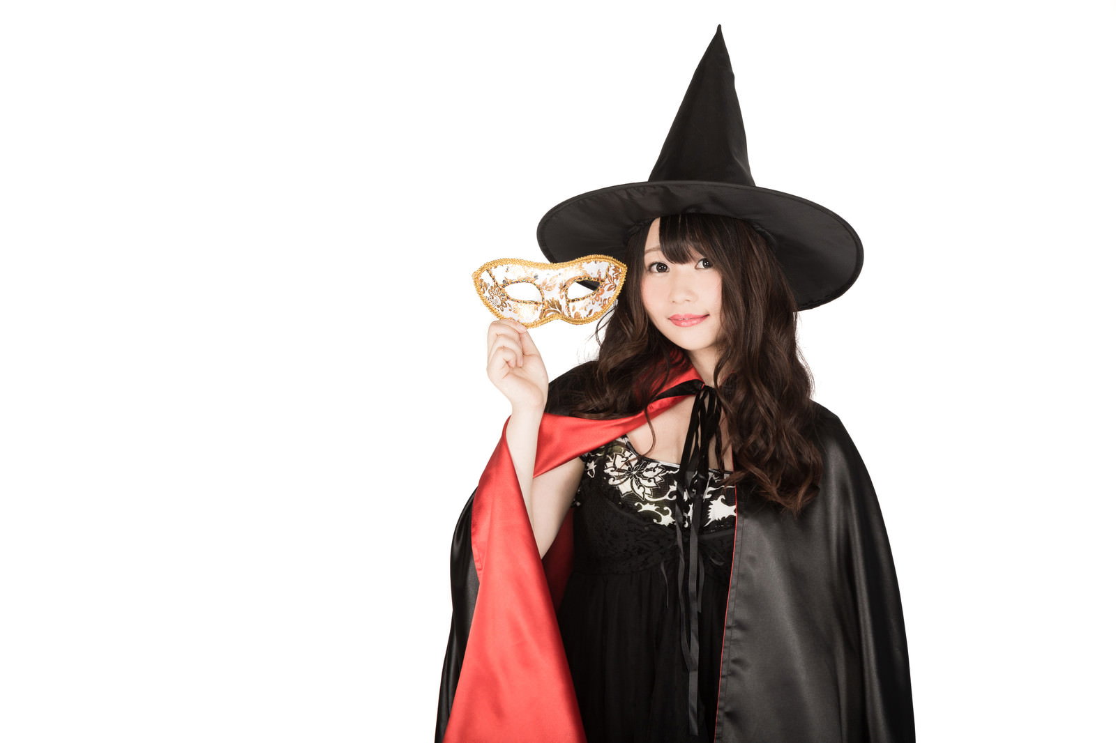 魔女の仮装をした女性が金色の仮面を持っている［モデル：茜さや］