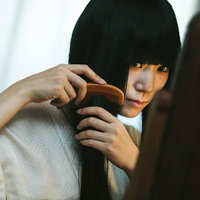 鏡に映る長い黒髪を櫛でとかす女性の美容シーンの写真