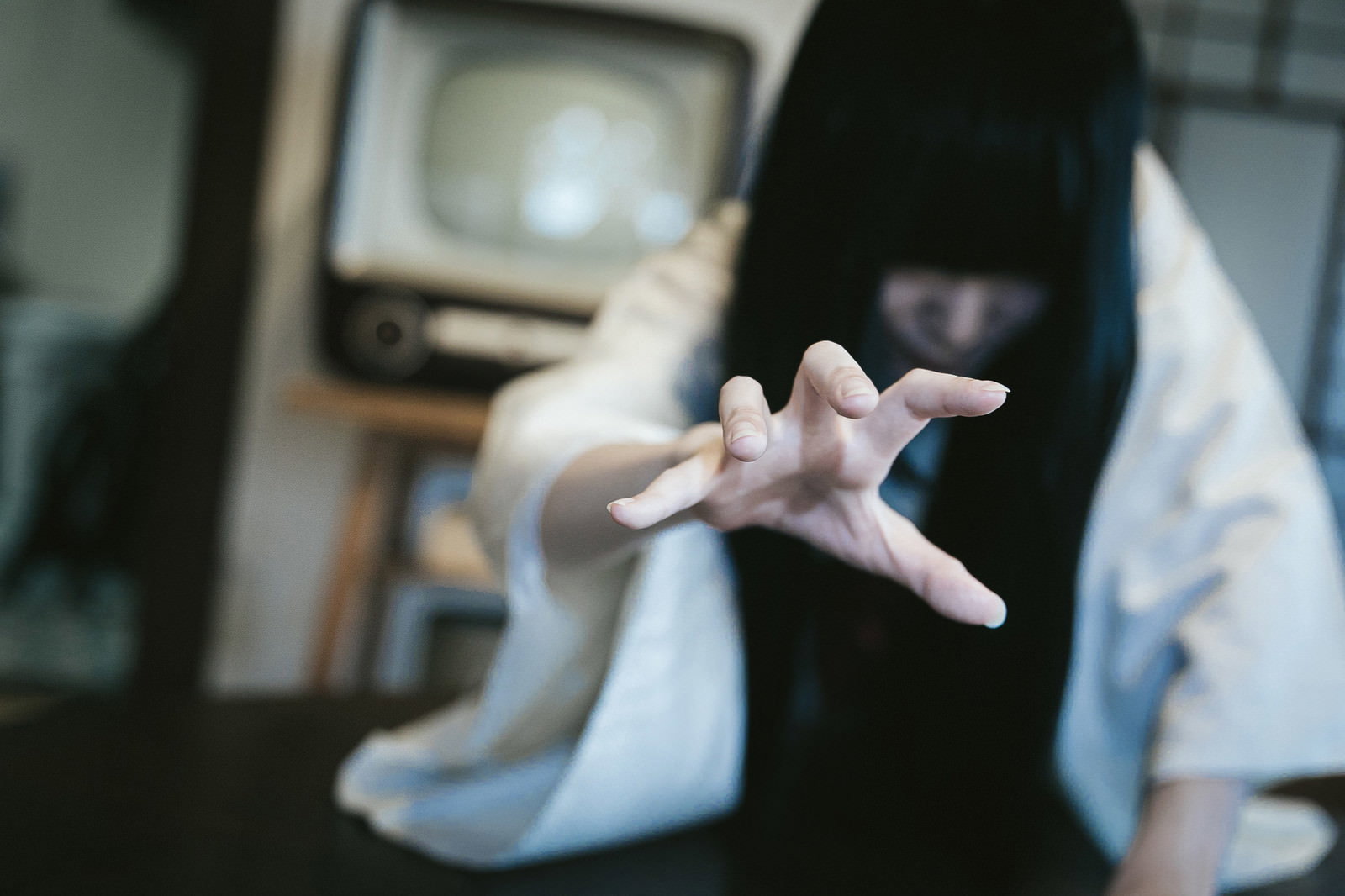 薄暗い部屋で古いテレビから這い出てくる長い黒髪の女性［モデル：緋真煉］