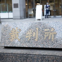 裁判所の入り口を警備する制服姿の警備員と石製看板の写真