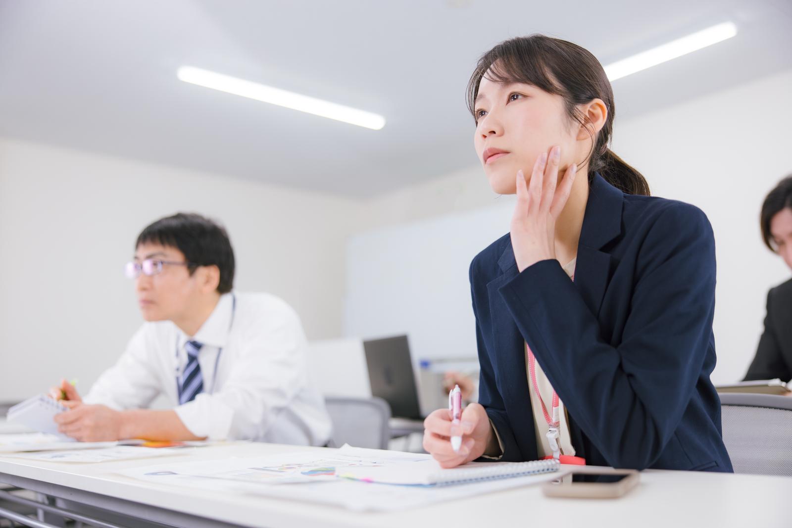 オフィスの会議室で頬杖をつきながら資料を確認するビジネスウーマン［モデル：SAKI］