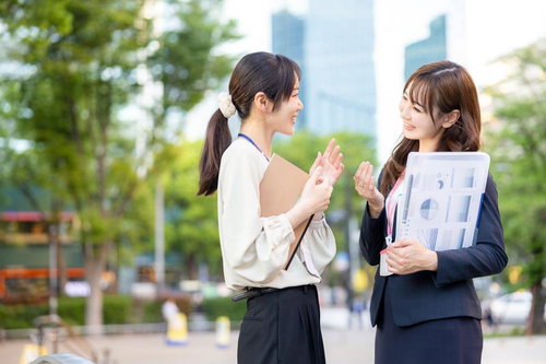資料をもって立ち話をする女性社員ふたり、ビジネス打ち合わせ