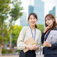 高層ビルを背景に資料を持つビジネスウーマンふたりの写真
