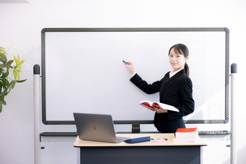 ホワイトボードの前で生徒に顔を向けて指導する女性講師