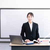 黒いスーツの女性講師がホワイトボードの前で授業を行う講師の写真