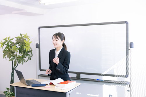 何も書かれていないホワイトボードの前でやる気を示す女性講師