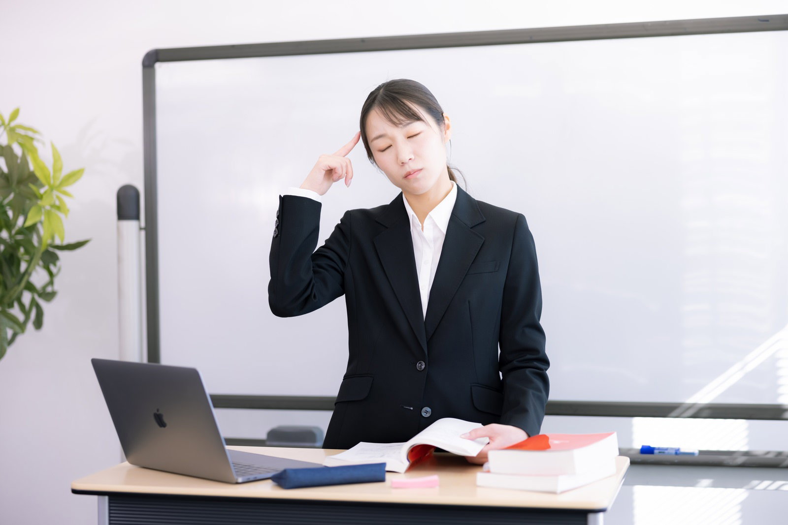 黒いスーツを着た女性講師が手を頭に当てて悩んでいる様子［モデル：SAKI］