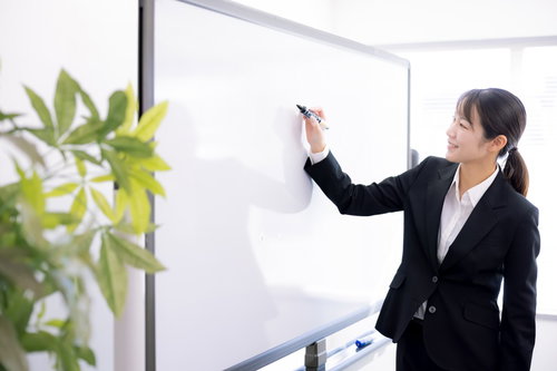 ホワイトボードに黒いマーカーで記入する女性講師