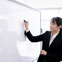 笑顔でホワイトボード前に立つ女性講師の講演の写真