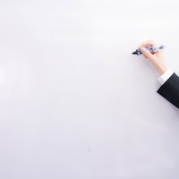 スーツ姿でペンを握る手とホワイトボードに書くの写真