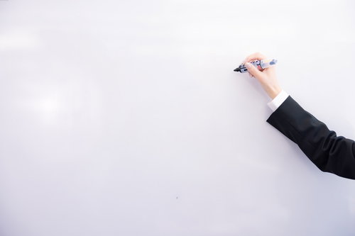 スーツ姿でペンを握る手とホワイトボードに書く