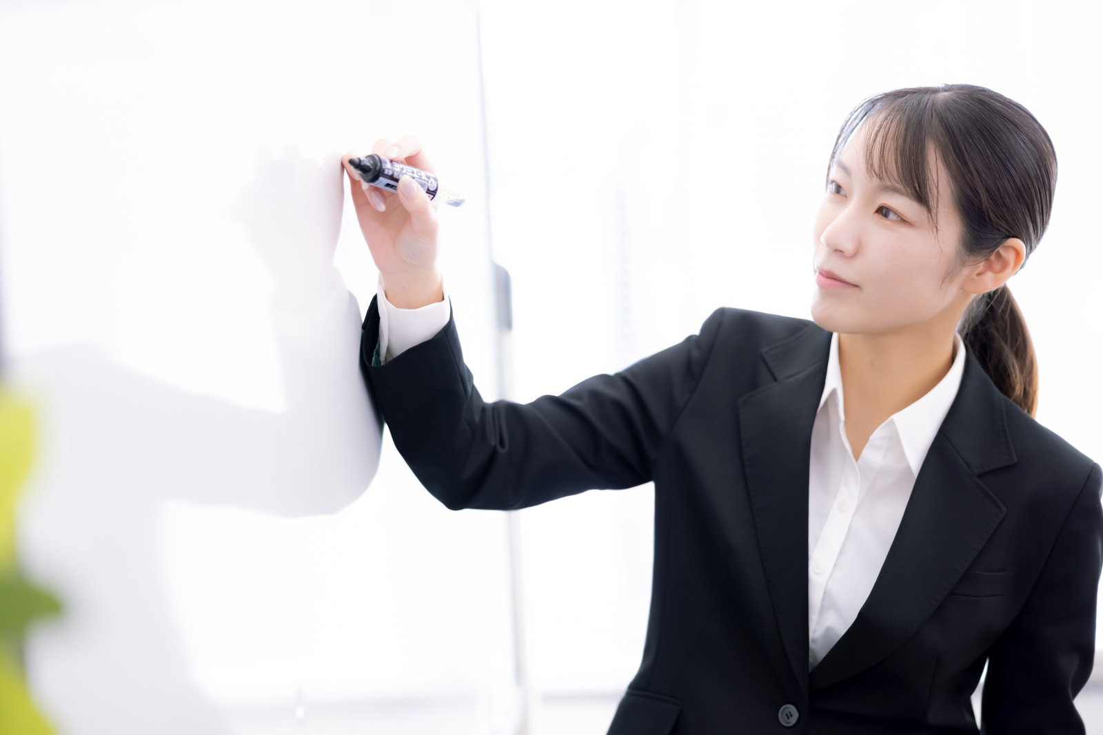 ホワイトボードに書いて説明する女性社員［モデル：SAKI］