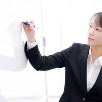ホワイトボードに書いて説明する女性社員のプレゼンテーションの写真