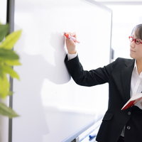 ホワイトボードを使って説明する授業中の若い女性の先生の写真