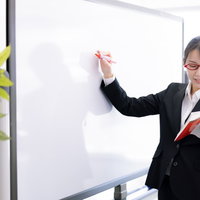 教科書に目を落とす女性講師がセミナーで説明している場面の写真