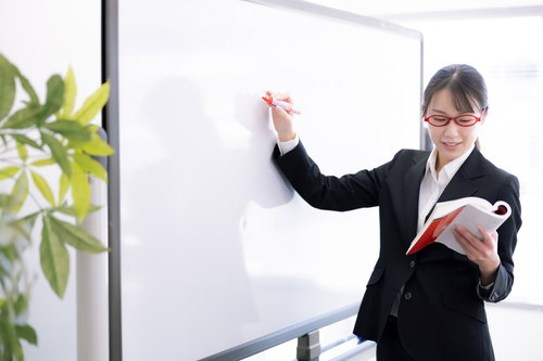 教科書に目を落とす女性講師がセミナーで説明している場面