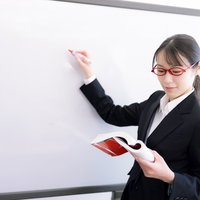 ホワイトボードの前でプレゼンする赤い眼鏡の女性の写真