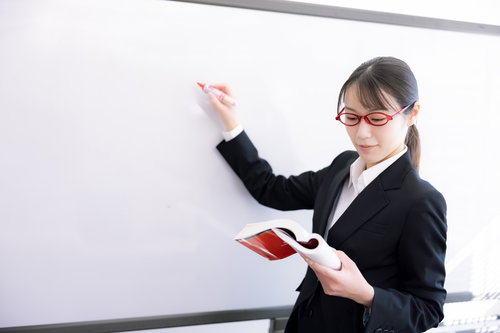 ホワイトボードの前でプレゼンする赤い眼鏡の女性