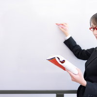 ホワイトボード前で赤い教材を手に取る女性講師の写真