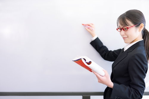 ホワイトボード前で赤い教材を手に取る女性講師