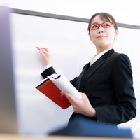 女性講師を見つめる受講者の目線、セミナーでのホワイトボード説明風景の写真