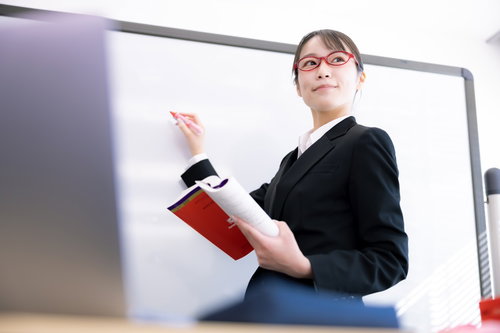 女性講師を見つめる受講者の目線、セミナーでのホワイトボード説明風景