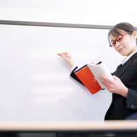 教材をホワイトボードに書き写す女性講師による授業風景の写真