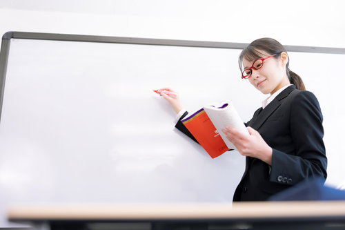 教材をホワイトボードに書き写す女性講師による授業風景