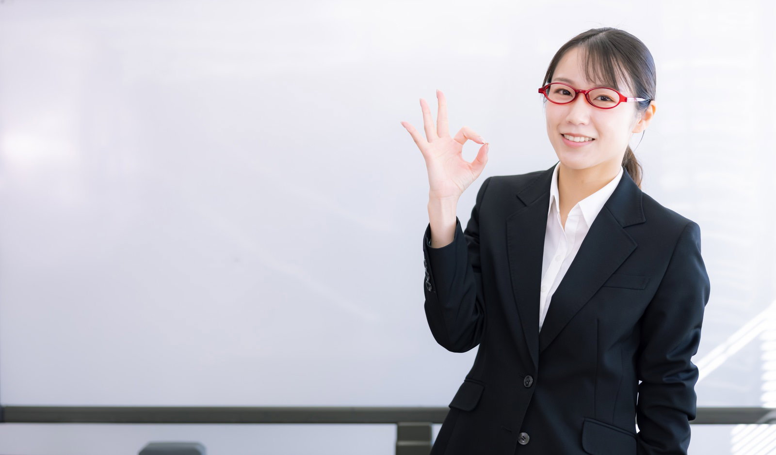 黒いスーツを着た女性がOKサインをしている様子とホワイトボード［モデル：SAKI］